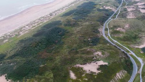 Aerial view of a coastal landscape with lush greenery, sandy dunes, and a winding road running