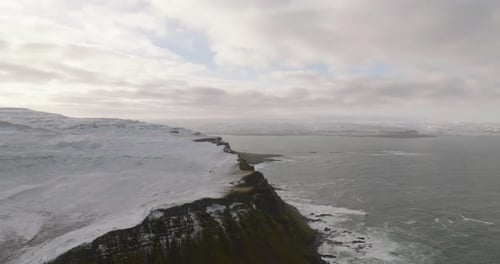 scenic icelandic landscape view on rocky shore ocean, snowy mountains and green grass