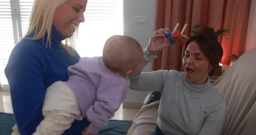 Two Women Entertain Baby with Wooden Toy Indoors