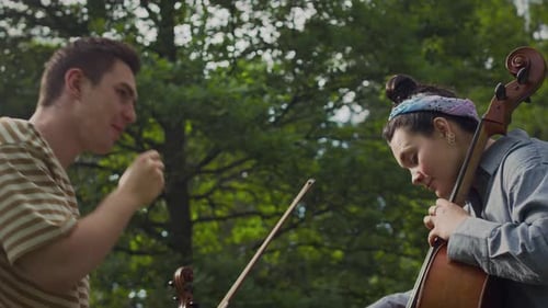 Une fille joyeuse jouant du violoncelle en tant que son amie fait du beatboxing dans un parc
