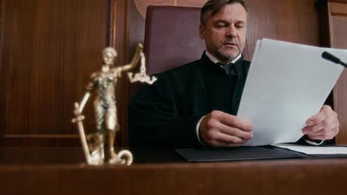 Judge Reviewing Documents at Table with Small Statue of Lady Liberty in Court