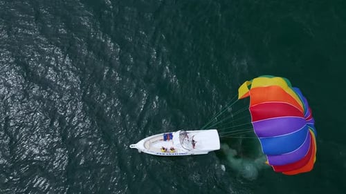 Drohnenvideo eines farbenfrohen Parasailers, der von einem Schnellboot über den Ozean gezogen wird. Die Szene fängt das ein