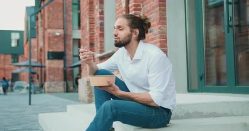 Business man in white shirt eating healthy salad on a break sitting on stairs over office building b