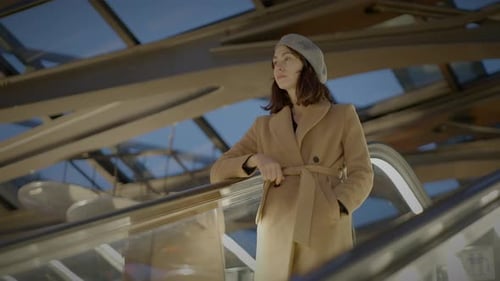 A Stylish Woman Wears a Beige Coat and Beret Posing in Front of a Modern Architectural Building