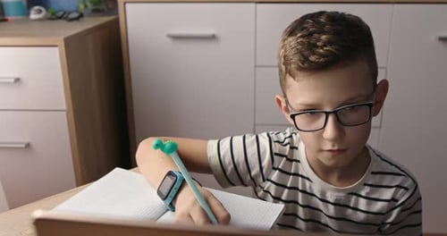 Young Boy Studying at Desk Writing in Notebook