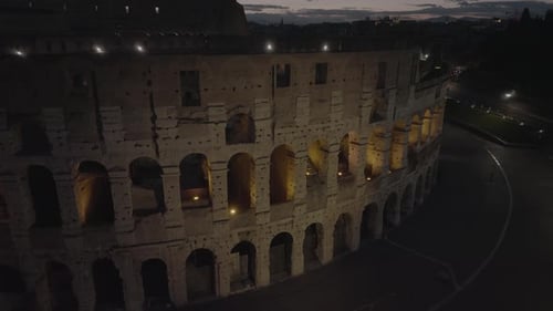 Aerial view of details of the illuminated Colosseum wall, night in Rome, Italy - ascending, tilt,