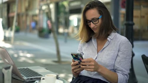 Young Businesswoman Texting on Smartphone Sitting in Cafe in City 30s