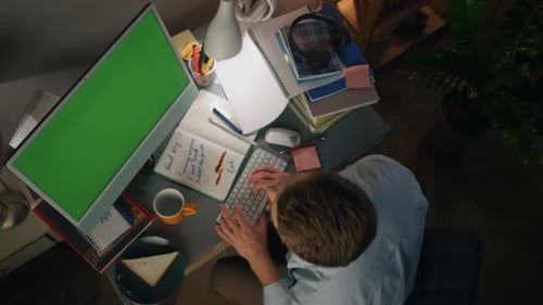 Serious freelancer typing on chromakey computer in apartment at night top view