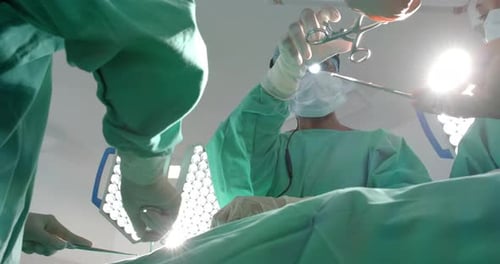 Diverse surgeons wearing surgical gowns operating on patient in operating theatre, slow motion