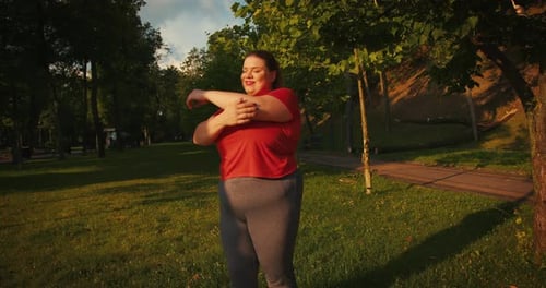 Woman Stretching Arms in Grassy Park at Sunrise
