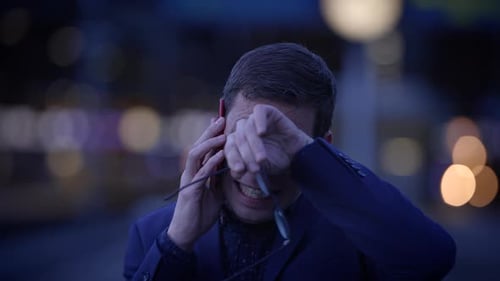 In an Urban Night Setting a Stressed Businessman is on a Phone Call Showcasing Visible Frustration