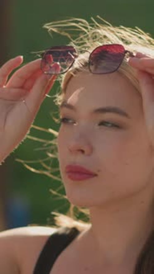 Une femme confiante ajuste ses lunettes de soleil à l'extérieur lorsque la lumière du soleil se reflète sur elle