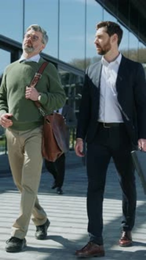 Two Goodlooking Male Colleagues Walking Near Business Center Talking and Gesturing Front View of