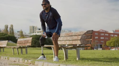 Athlete with Artificial Leg Drinking Water on Bench in Park