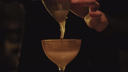 Bartender Pours Cocktail Through Strainer into Glass