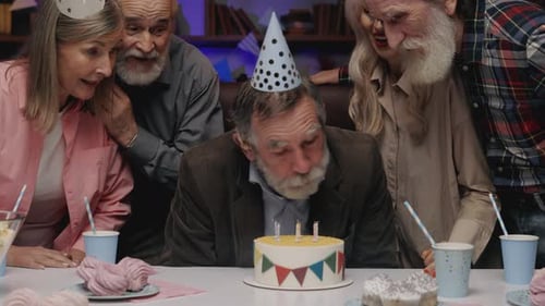 Elderly Man Blowing Out Candles at Birthday Party
