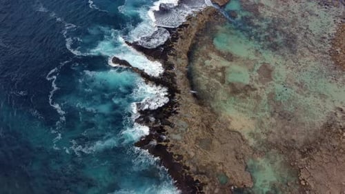 Vue aérienne des vagues qui s'écrasent sur les récifs coralliens, eau turquoise et rivage rocheux visibles