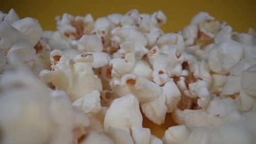 Slow dolly shot of falling popcorns in slow motion in front of yellow background,close up