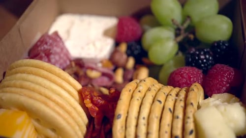 Une boîte à snacks à charcutterie avec de la charcuterie cuite, des craquelins, des raisins, des baies et du fromage, en rotation