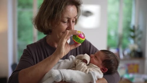 Mature Woman Holds Infant and Plays with Toy