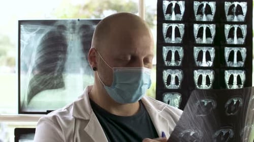 Radiologist doctor with face mask examining an Xray film, profile view
