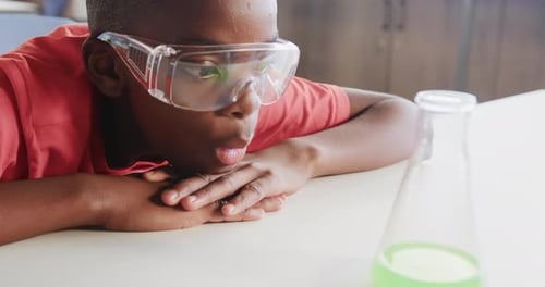 In school, boy wearing safety goggles observing green liquid in beaker