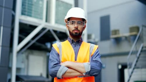 Portrait of confident professional engineer wearing safety helmet, protective glasses and vest stand