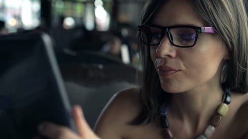Young Woman with Glasses Using Tablet Computer Sitting in Cafe 30s