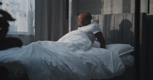 Dans une chambre moderne, un homme adulte se réveille dans un lit blanc