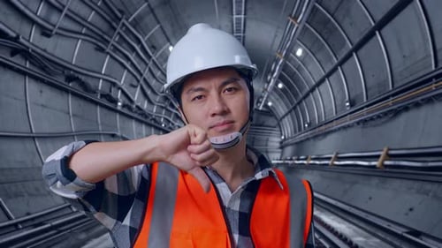 Asian Male Engineer Showing Thumbs Down Gesture And Shaking His Head In Subway Tunnel