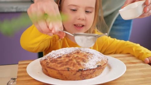 Girl Sprinkles Sugar on Cake with Adult