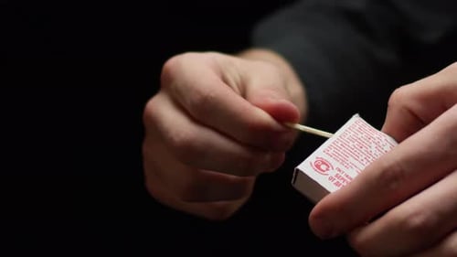 Man Strikes Match Holding Small Box on Black Background
