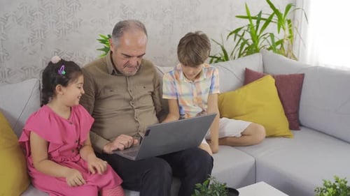 Grandfather Using Laptop With Grandchildren on Couch