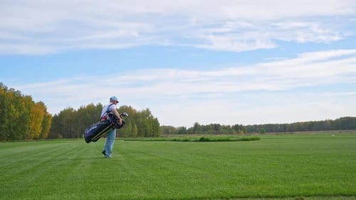 A Man is Leisurely Walking on a Beautiful Golf Course While Carrying His Golf Equipment with Him