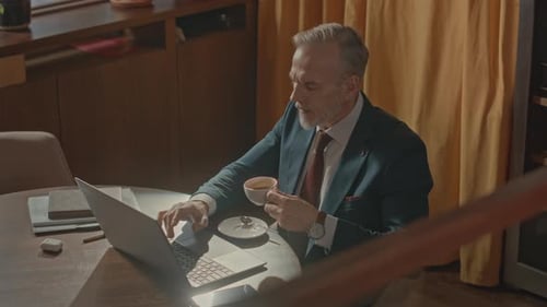 Professional Using Laptop and Drinking Coffee Indoors