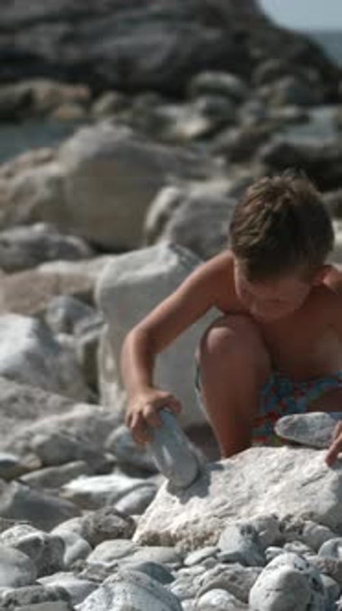 A Little Boy is Playing with Rocks on the Beach Creative A Child Sitting Next to the Sea Who is