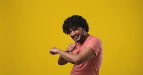 Young Indian Bearded Guy with Curly Hair Wearing Tshirt Dancing Over Orange Studio Background