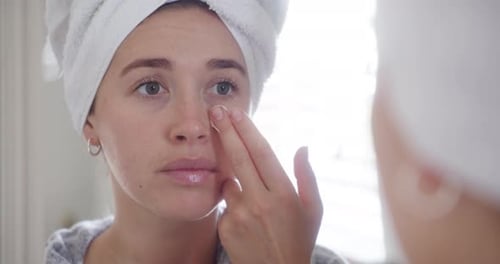 Woman Applying Facial Cream in Bathroom Mirror