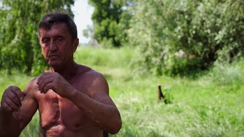 Shirtless Man Practices Boxing Punches in Field