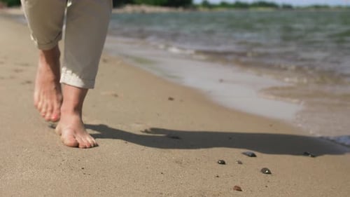 Woman feet walking barefoot along summer beach coastline slow motion