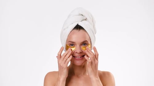 Woman Smiling Applying Gold Eye Patches in Bathroom