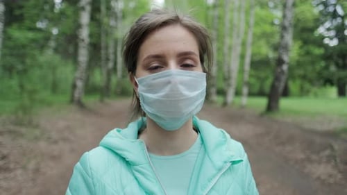 Woman in mask in the park. Young pretty woman stands in the park with protective mask and looks at t