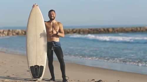 Surfer Leans on Surfboard on Beach