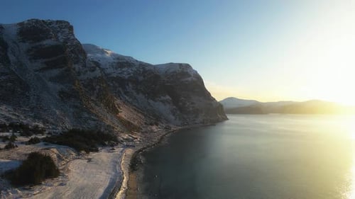 Golden Hour Sunlight Reflecting Over Snowy Arctic Fjord Coastal Mountains