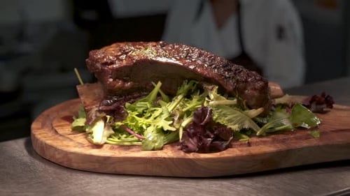 Plated beef rib roast over greens on wood carving board in commercial restaurant kitchen, HD