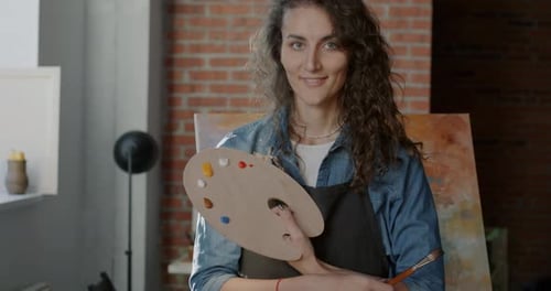 Portrait of Beautiful Young Lady Artist Standing in Studio Holding Color Palette and Brush Smiling