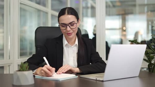 Successful Female Writing Information From Computer to Notebook in Office