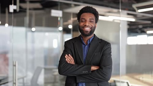 Confident Young Businessman Smiles with Arms Crossed in a Modern Office