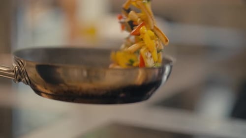 Chef frying vegetables in hot pan, close up