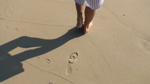 Woman walking on a sandy beach leaving footprints in super slow motion